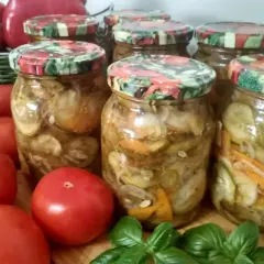 Słoiki z ogórkami w zalewie gyros, obok pomidory i bazylia.