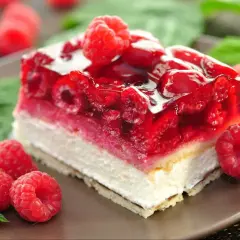 Pyszne ciasto z malinami, z galaretką i bitą śmietaną, ozdobione świeżymi malinami.
