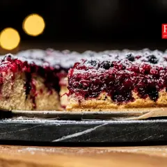 Pyszne ciasto z porzeczkami, posypane cukrem pudrem, prezentuje się apetycznie na kamiennej tacy.