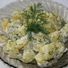Pyszna sałatka ziemniaczana z koperkiem i ogórkiem kiszonym, podana w szklanej misie.