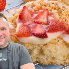 Uśmiechnięty mężczyzna w fartuchu prezentuje pyszne drożdżówki z truskawkami, posypane kruszonką i polane lukrem.