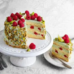 Pyszny tort pistacjowo malinowy, udekorowany świeżymi malinami i pistacjami, kusi swoim wyglądem i smakiem.