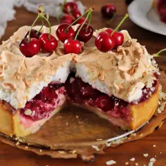 Pyszna tarta z czereśniami, udekorowana bezą i płatkami migdałów, kusi soczystym nadzieniem.