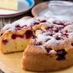 Wilgotne ciasto z wiśniami, posypane cukrem pudrem, wygląda apetycznie. Kawałek ciasta na talerzyku obok.
