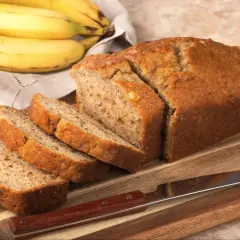 Pyszny chlebek bananowy bez cukru, pokrojony na kromki, leży na desce obok pęczka bananów.