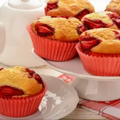 Pyszne muffinki z truskawkami w różowych papilotkach, obok białego dzbanka. Idealne na deser.