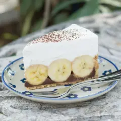 Pyszne ciasto bananowe bez pieczenia z kremową pianką i bananami na wierzchu, posypane kakao. Idealne na deser.