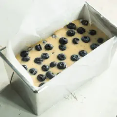 Surowe ciasto z borówkami w metalowej formie wyłożonej papierem do pieczenia.
