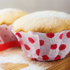 Puszyste babeczki z budyniem, posypane cukrem pudrem, w papierowych foremkach w czerwone kropki.