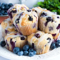 Stos pysznych muffinek z borówkami, polanych lukrem, ozdobiony świeżymi owocami.