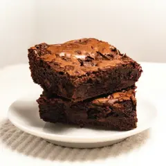 Dwa wilgotne, czekoladowe brownie ułożone jedno na drugim na białym talerzyku. Idealne na deser, zgodnie z prostym brownie przepis.