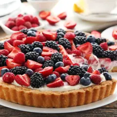 Pyszna tarta z owocami: malinami, borówkami, jeżynami i truskawkami, udekorowana kremem.