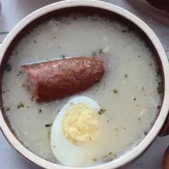 Aromaticzny żurek z kiełbasą i jajkiem, przygotowany na bazie domowego zakwasu na żurek. Obok czosnek, cebula i jajka.