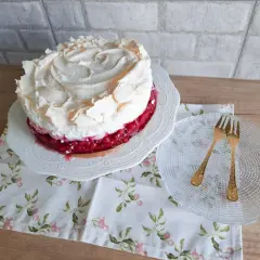 Pyszna tarta z porzeczkami, udekorowana puszystą bezą. Obok talerzyk z dwoma złotymi widelczykami.