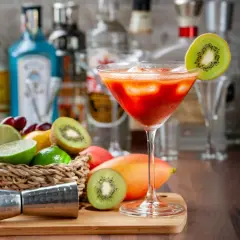 Koktajl z kiwi i mango, idealny do nauki, jak zrobić nalewkę. Na blacie stoją owoce, jigger i butelki alkoholu.