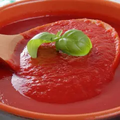 Gęsty, czerwony ketchup z pomidorów, nabierany drewnianą łyżką, ozdobiony listkiem bazylii.