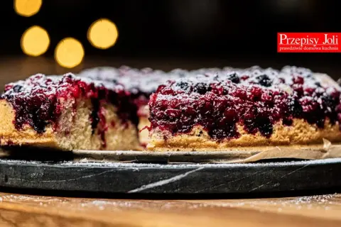 Pyszne ciasto z porzeczkami, posypane cukrem pudrem, prezentuje się apetycznie na kamiennej tacy.