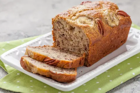 Pyszny chlebek bananowy fit z orzechami pekan i plasterkami banana na wierzchu, pokrojony na talerzu.