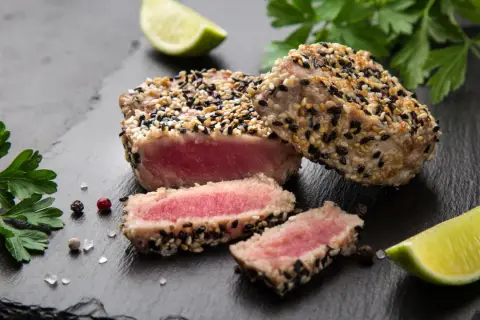 Apetyczny stek z tuńczyka w sezamie, idealnie wysmażony, z kawałkami limonki i natką pietruszki.