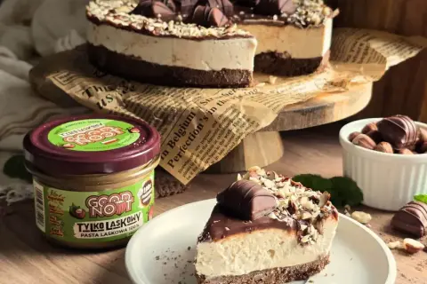 Pyszne ciasto z mascarpone, udekorowane czekoladą i orzechami. Obok słoik pasty z orzechów laskowych.