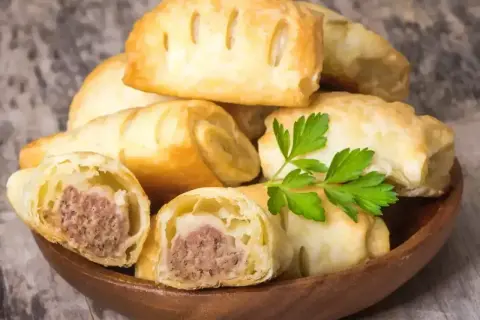 Stos pieczonego ciasta francuskiego z kiełbasą, ozdobiony natką pietruszki. Idealne na szybką przekąskę.