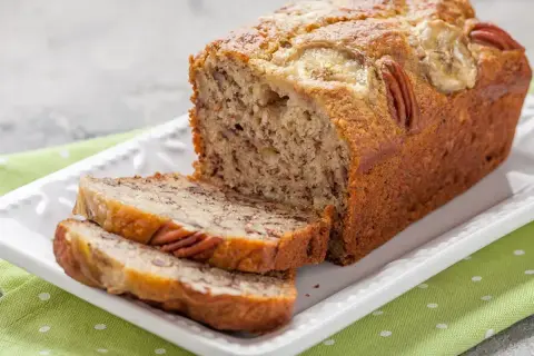 Pyszny chlebek bananowy z orzechami pekan i plasterkami banana na wierzchu, pokrojony na kromki.