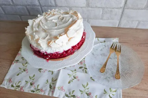 Pyszna tarta z porzeczkami, udekorowana puszystą bezą. Obok talerzyk z dwoma złotymi widelczykami.