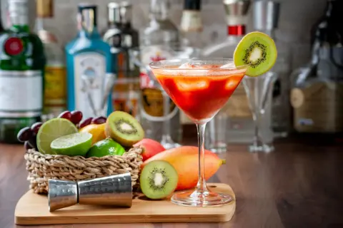Koktajl z kiwi i mango, idealny do nauki, jak zrobić nalewkę. Na blacie stoją owoce, jigger i butelki alkoholu.