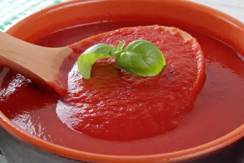 Gęsty, czerwony ketchup z pomidorów, nabierany drewnianą łyżką, ozdobiony listkiem bazylii.