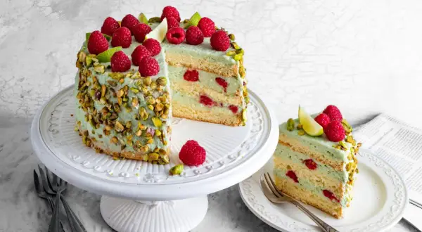 Pyszny tort pistacjowo malinowy, udekorowany świeżymi malinami i pistacjami, kusi swoim wyglądem i smakiem.