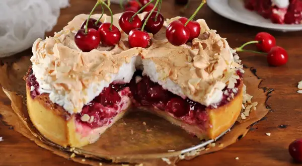 Pyszna tarta z czereśniami, udekorowana bezą i płatkami migdałów, kusi soczystym nadzieniem.