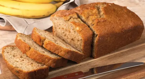 Pyszny chlebek bananowy bez cukru, pokrojony na kromki, leży na desce obok pęczka bananów.