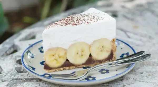 Pyszne ciasto bananowe bez pieczenia z kremową pianką i bananami na wierzchu, posypane kakao. Idealne na deser.