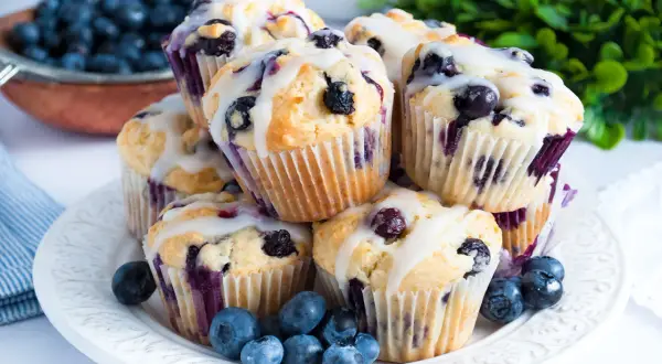 Stos pysznych muffinek z borówkami, polanych lukrem, ozdobiony świeżymi owocami.