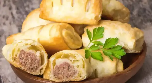 Stos pieczonego ciasta francuskiego z kiełbasą, ozdobiony natką pietruszki. Idealne na szybką przekąskę.