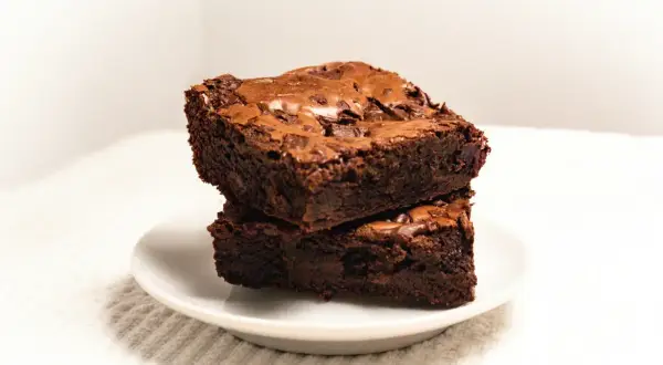 Dwa wilgotne, czekoladowe brownie ułożone jedno na drugim na białym talerzyku. Idealne na deser, zgodnie z prostym brownie przepis.