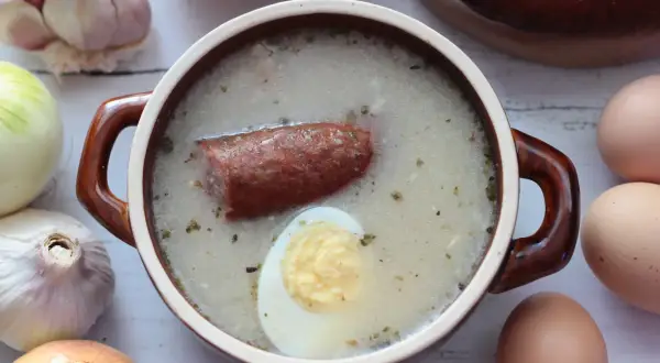 Aromaticzny żurek z kiełbasą i jajkiem, przygotowany na bazie domowego zakwasu na żurek. Obok czosnek, cebula i jajka.