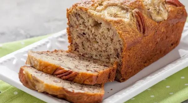 Pyszny chlebek bananowy z orzechami pekan i plasterkami banana na wierzchu, pokrojony na kromki.