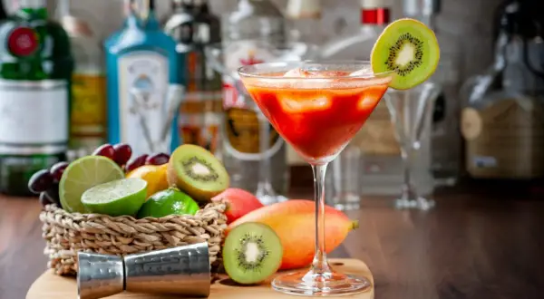 Koktajl z kiwi i mango, idealny do nauki, jak zrobić nalewkę. Na blacie stoją owoce, jigger i butelki alkoholu.