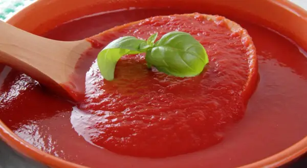 Gęsty, czerwony ketchup z pomidorów, nabierany drewnianą łyżką, ozdobiony listkiem bazylii.