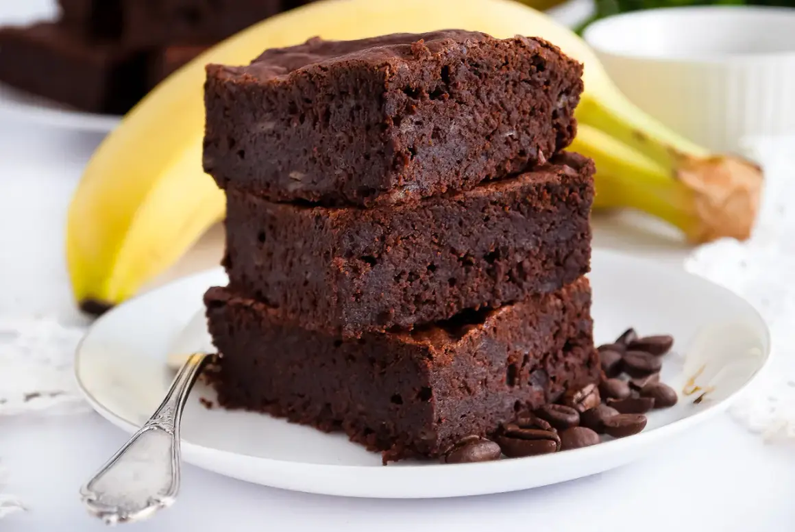 Stos pysznych brownie z bananami, ozdobiony ziarnami kawy, na talerzu z widocznym bananem w tle.
