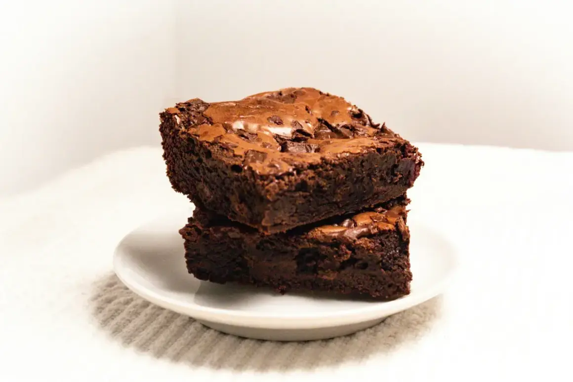 Dwa wilgotne, czekoladowe brownie ułożone jedno na drugim na białym talerzyku. Idealne na deser, zgodnie z prostym brownie przepis.