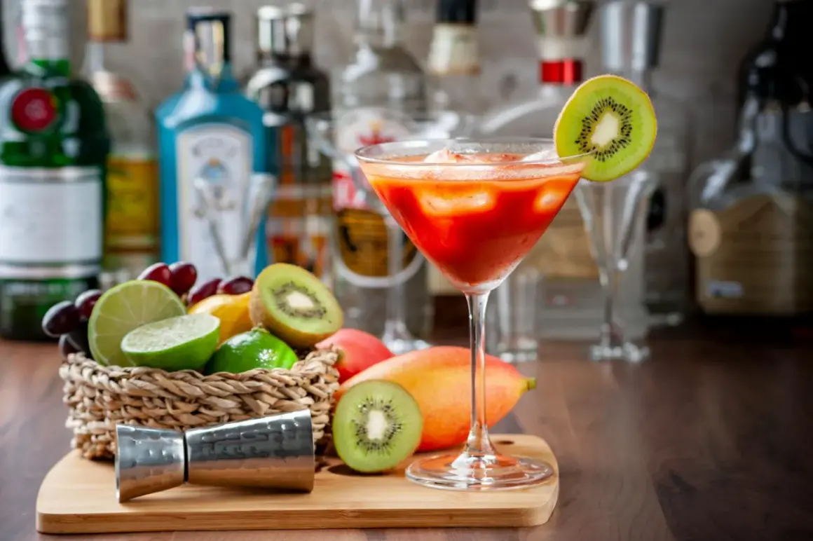 Koktajl z kiwi i mango, idealny do nauki, jak zrobić nalewkę. Na blacie stoją owoce, jigger i butelki alkoholu.