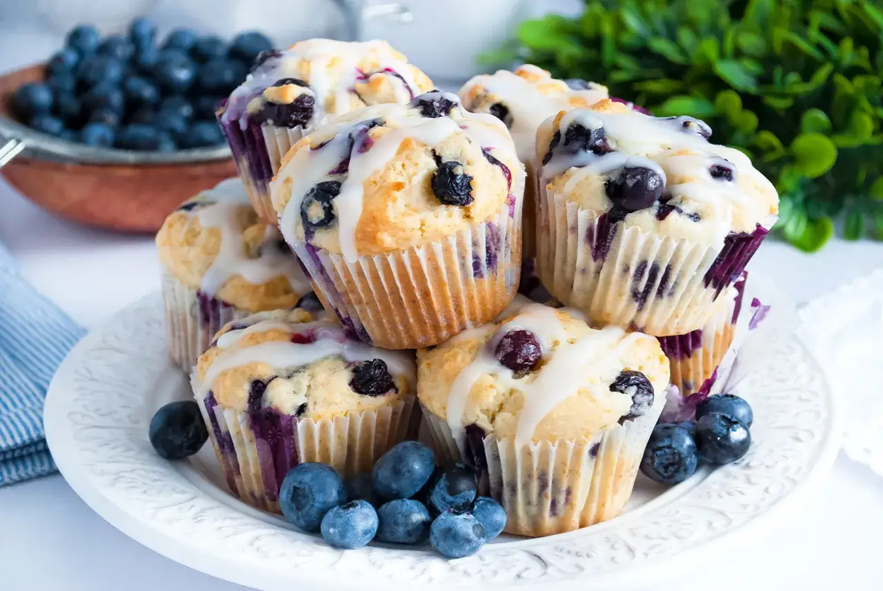 Stos pysznych muffinek z borówkami, polanych lukrem, ozdobiony świeżymi borówkami.