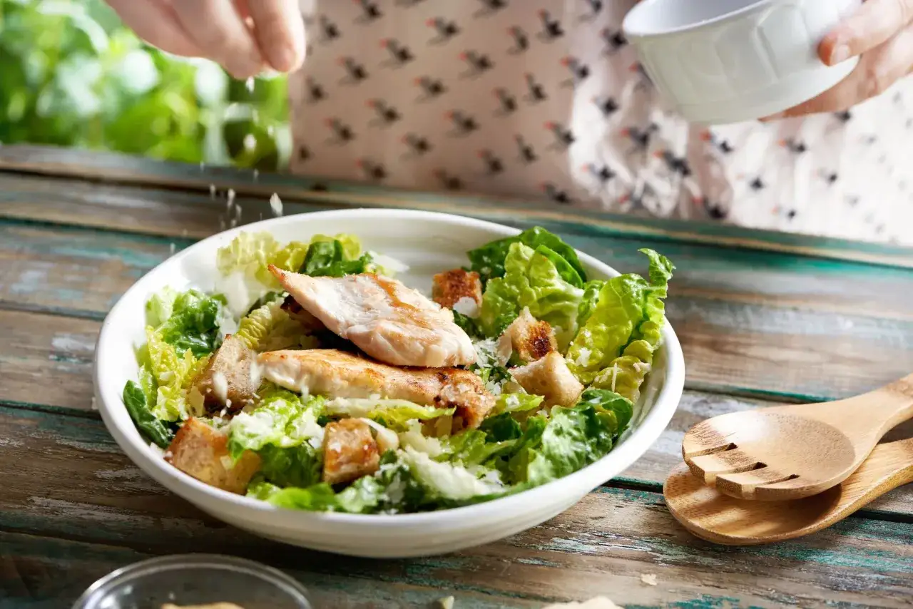 Pyszna sałatka cezar z grillowanym kurczakiem i chrupiącymi grzankami, posypana parmezanem.