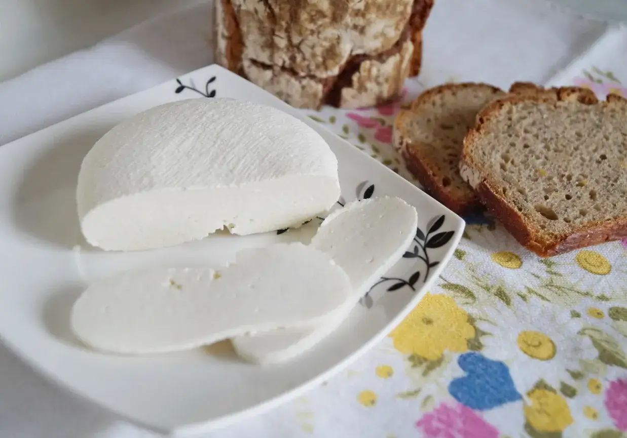 Domowy twaróg z mleka krowiego, pokrojony w plastry, podany z chlebem. Prosty przepis na pyszny ser.