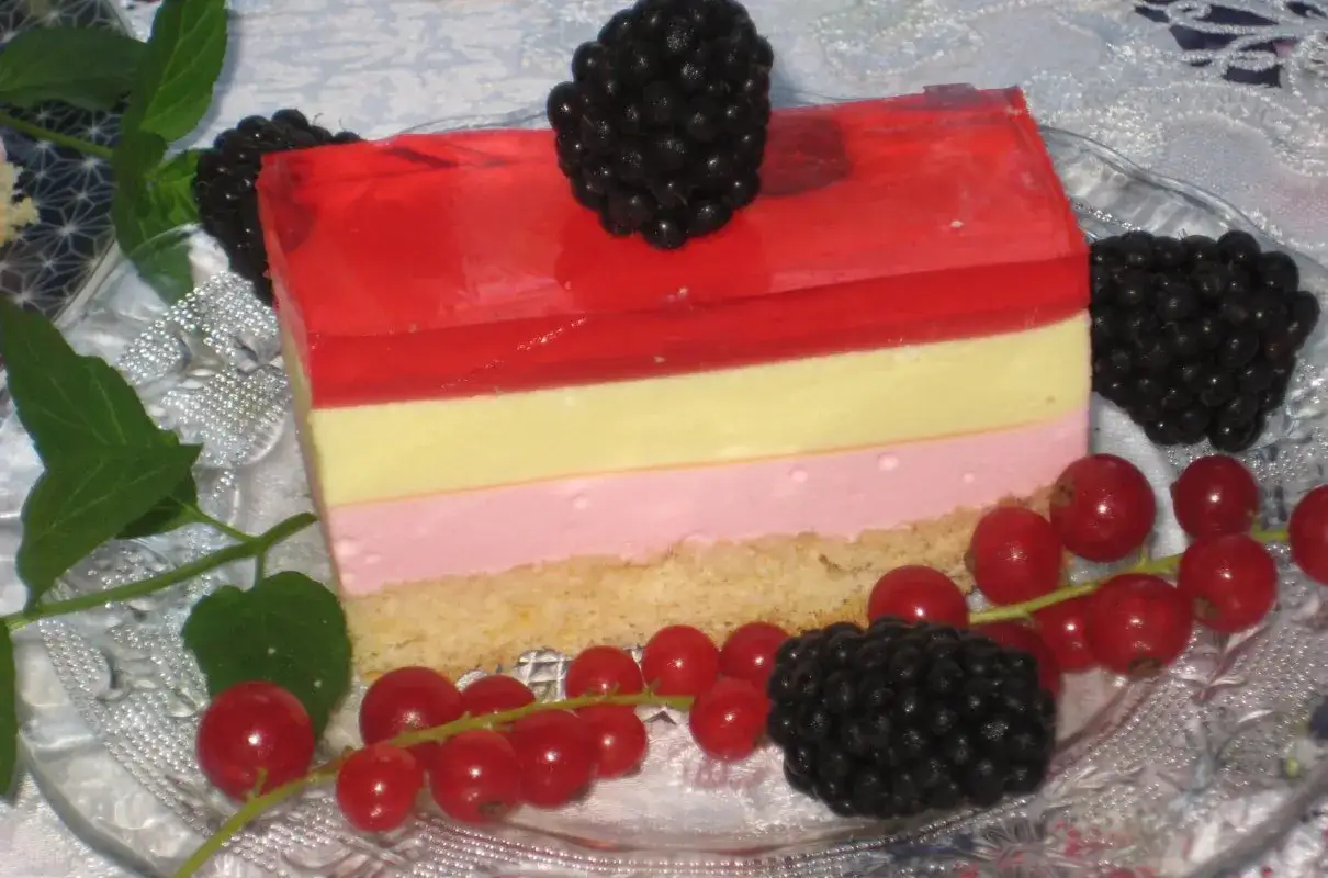 Pyszne ciasto ptasie mleczko z warstwami galaretki i kremu, ozdobione jeżynami i porzeczkami.