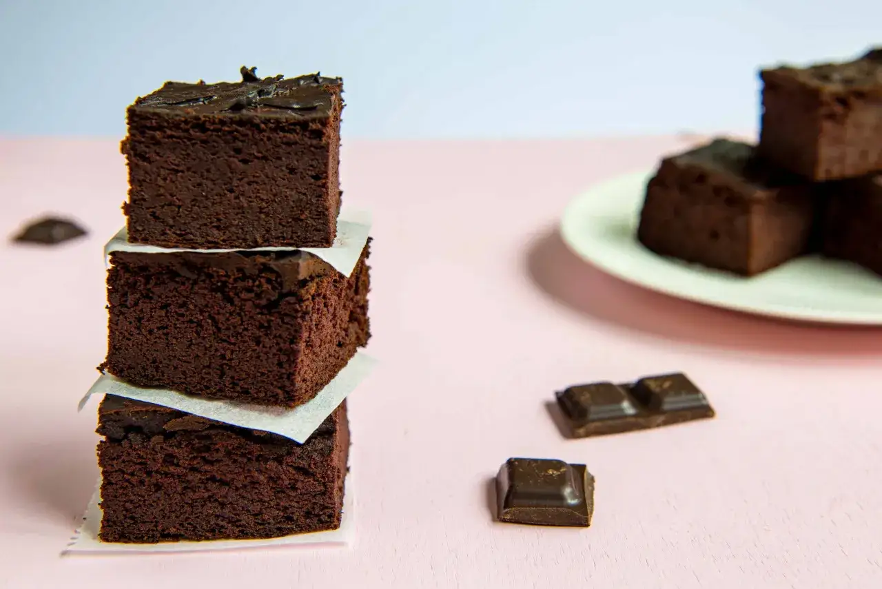 Ciemne, wilgotne brownie z fasoli, ułożone w wieżę, obok kawałk&oacute;w czekolady.