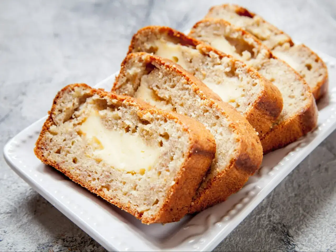 Pokrojony chlebek bananowy bez cukru z kremowym nadzieniem, ułożony na białej paterze.