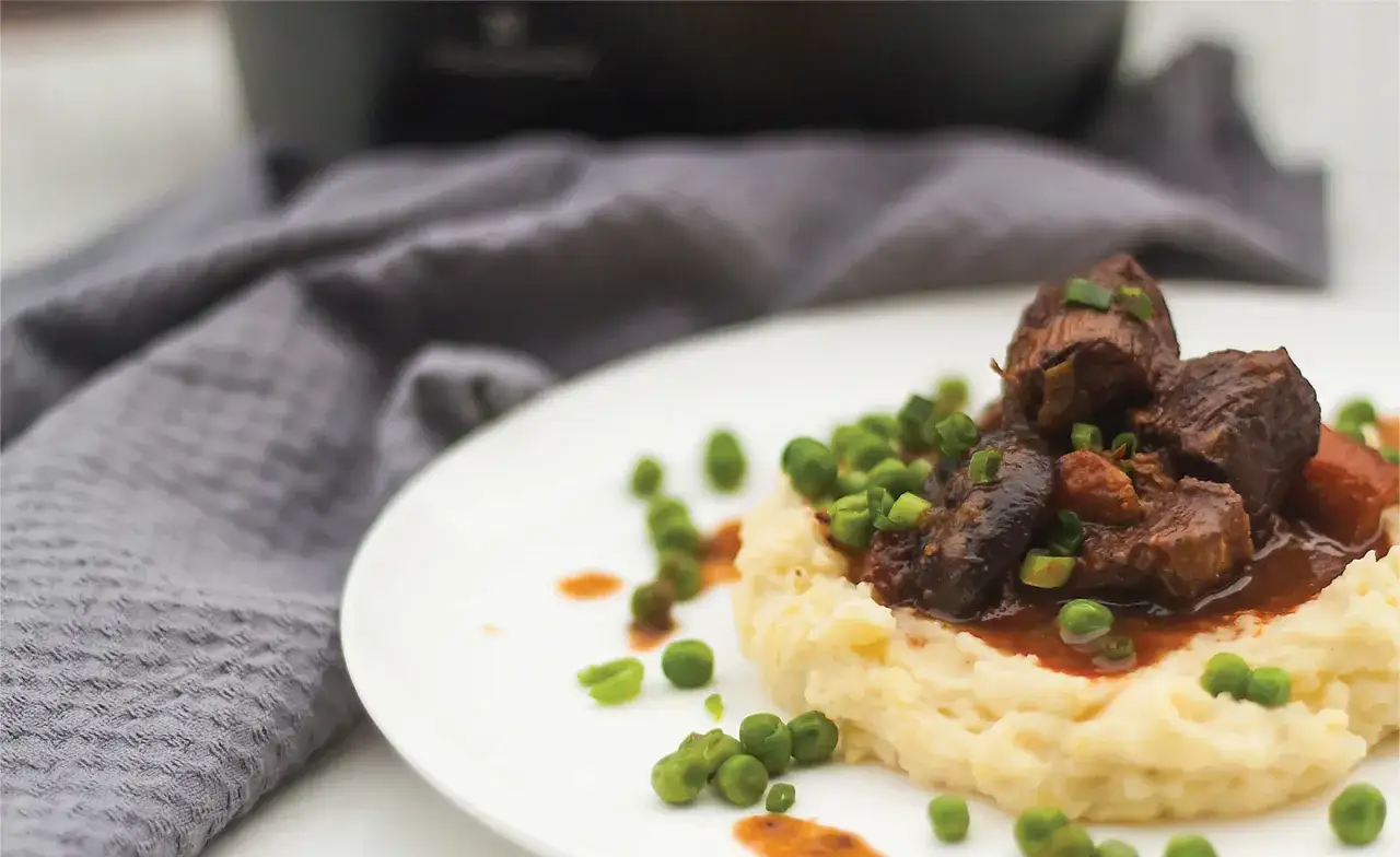 Pyszne wołowina po burgundzku na kremowym purée, posypana zielonym groszkiem i szczypiorkiem.
